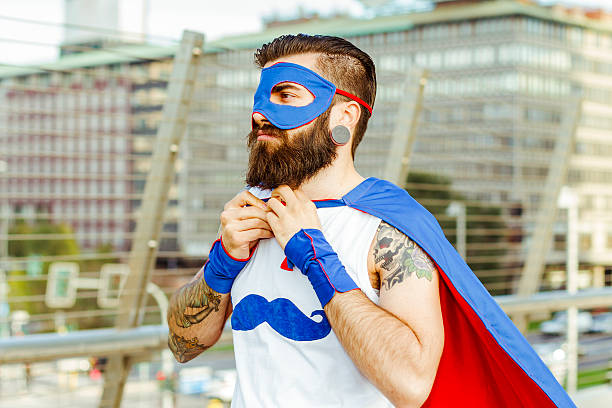 Hipster superhero adjusting his mantle Portrait of Young man (hipster style) with big earring and full beard with a superhero costume. Adjusting the mantle. cosplay stock pictures, royalty-free photos & images