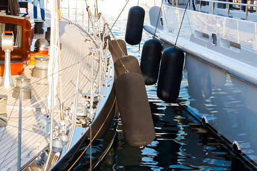 Closeup luxury yachts fenders, device for protecting the side of a sailing vessel as it heads into port, with reflection of water on side of the yacht, full frame horizontal composition