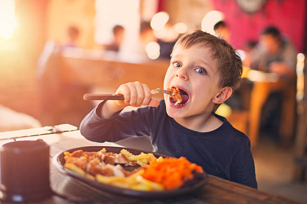 Little boy enjoying dinner at the restaurant Little boy having fun eating a dinner in the restaurant. Little boy is wearing a dark blouse and earing chicken, french fries and carrot salad. Slightly soft. kids restaurant pictures stock pictures, royalty-free photos & images