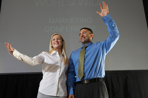 Man and woman waving from stage during business convention
