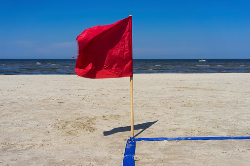 Red flag in the wind on the sandy beach with blue lines. Jurmala, Latvia