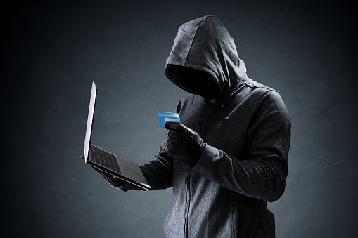 Computer hacker with credit card stealing data from a laptop concept for network security, identity theft and computer crime