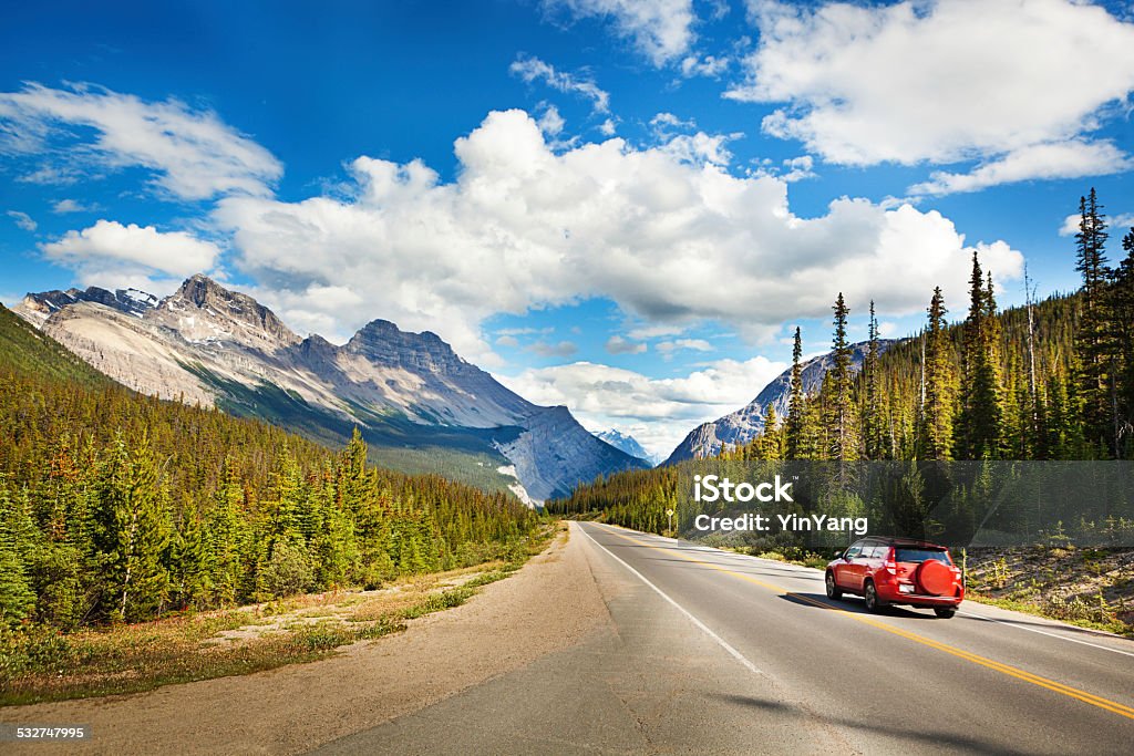 Banff National Park Road Trip Drive through Canadian Rocky Mountains Tourist red car taking a road trip, driving through Canadian Rockies, Banff National Park, Alberta, Canada. Summer vacation travelers seek North American scenic natural destinations to experience mountain range landscape views, snow-capped glacial peaks, majestic, tranquil wilderness areas, and beauty in nature. Sunny highway and cloudy sky provide copy space. Car Stock Photo