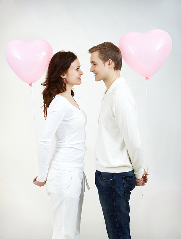 Two beautiful young people with heart-shaped balloons looking at each other