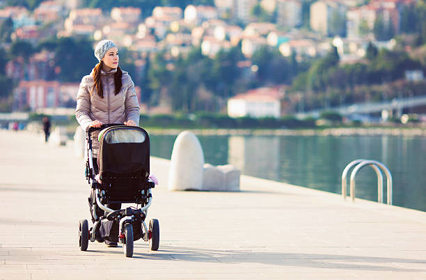 Young mother walking her baby in a stroller by the sea on a sunny day