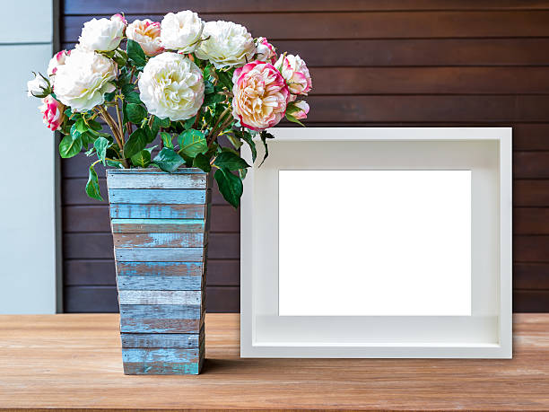 Blank white picture frame and flowers vase on wooden desktop stock photo
