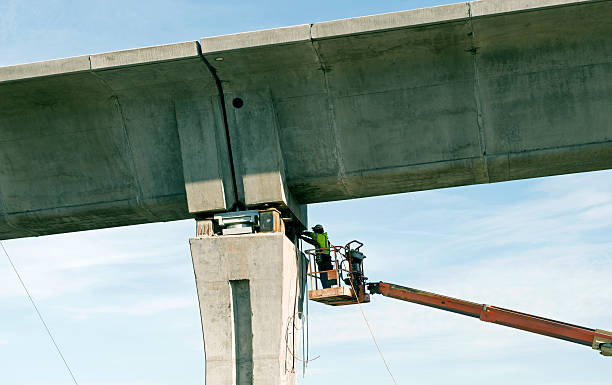 Worker levelling concrete piers on column with hydraulic machine Seattle, USA--13 January 2013: A worker levels concrete piers on columns with a hydraulic machine on a new light rail extension in winter in Seattle WA. light-rail-construction stock pictures, royalty-free photos & images