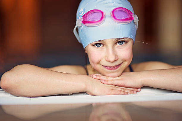 Portrait of a little girl in swimming pool Little girl smiling into the camera fron inside the swimming pool. She is wearing a blue swim cap and ping swim goggles. swimming cap stock pictures, royalty-free photos & images