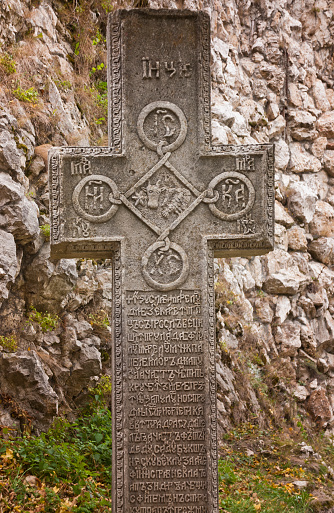 Old stone cross inscribed in ancient Slavic language at a Romanian heritage site.