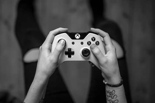 Gothenburg, Sweden - January 17, 2015: A black and white shot from above of a young woman's hands holding a white Xbox One controller as she is playing a video game. Natural lighting, shot on wooden background with shallow depth of field.