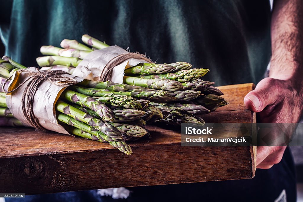 Farmer carries tied asparagus on a wooden board Asparagus. Raw asparagus. Fresh Asparagus.Green Asparagus. Tied asparagus in other positions. Farmer carries tied asparagus on a wooden board. Chef Stock Photo