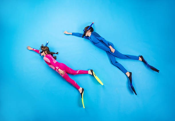 Child scuba divers Children scuba diving deep in the sea. Studio shot on a blue background. diving flippers stock pictures, royalty-free photos & images