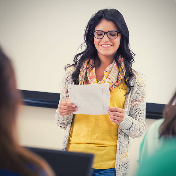 istock Pretty Hispanic student reading report to classmates near white board 532850039
