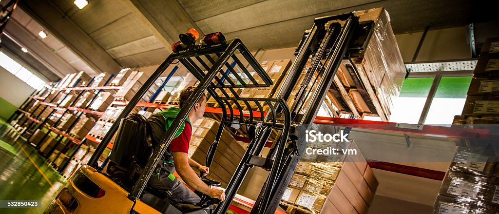 Forklift Operator Loading a Pallet Wide shot of warehouse worker lifting a pallet of goods with a forklift in a colorful warehouse setting. Low angle view. Forklift Stock Photo