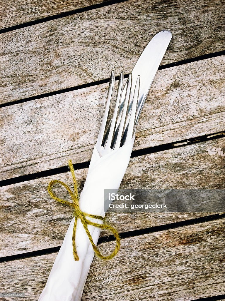 Rustic place setting A knife, fork and paper napkin tied together with string on a simple rustic table. 2015 Stock Photo