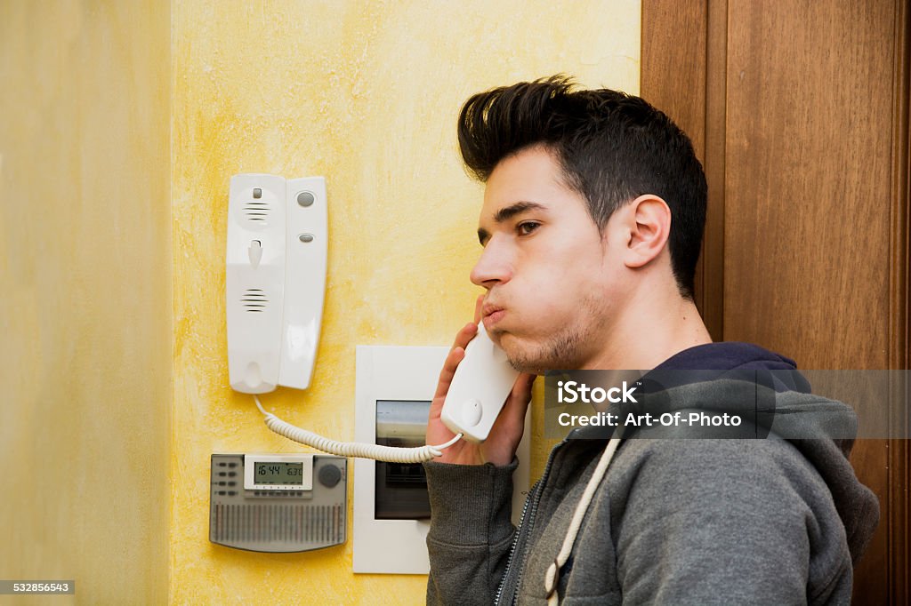 Teenager answering the intercom in an apartment Teenager answering the intercom at the entrance in an apartment blowing out his cheeks in frustration on finding an unwelcome visitor on the other end Intercom Stock Photo