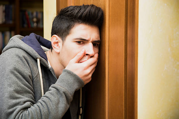 Young man listening in behind a door Young man listening in behind a door holding his hand to his mouth with a shocked expression at what he has overheard eavesdropping stock pictures, royalty-free photos & images