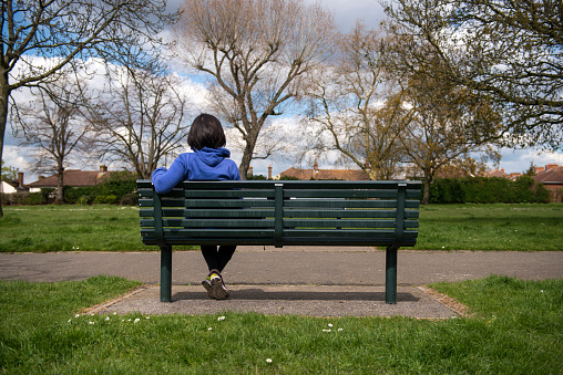 Woman sitting on bench with back turned looking at the park thinking