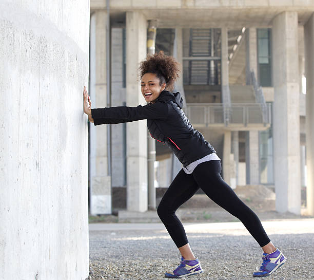un sorridente giovane donna sport stretching esercizio all'aperto - pushing women people wall foto e immagini stock