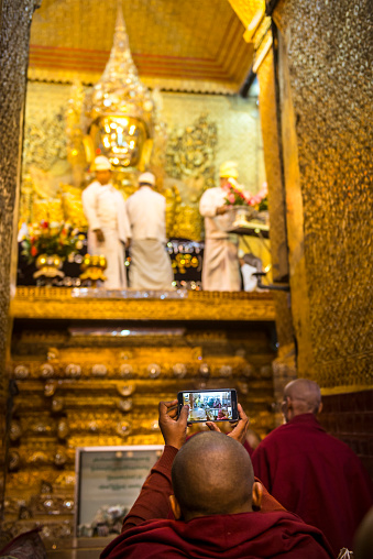 Mandalay, Myanmar- February 3, 2016: Buddhist monk in traditional robes is taking photo by Samsung smartphone at the Mahamuni Buddha Temple. Early morning ritual of face wash to Maha Myat Muni Buddha Image at Mahamuni Temple, Mandalay, Myanmar.