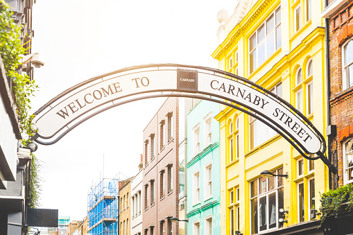 Carmaby street sign in London with some colorful houses on background and sun beams from top. This is a famous place in London, with many tourists visiting every day.