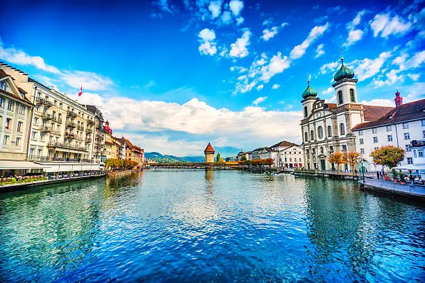 Beautiful Cityscape of old town Lucerne, visible are Jesuit Church, river Reuss waterfront of Lucerne with the famous Kapellbrucke bridge originally built in 1333, traditional swiss buildings, restaurants, coffee bars, hotels, beautiful cloudscape and reflection in the water.  