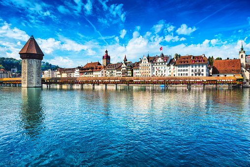 Beautiful Cityscape of old town Lucerne, visible are the river Reuss waterfront of Lucerne with the famous Kapellbrucke bridge originally built in 1333, traditional swiss buildings, churches, restaurants, coffee bars, hotels, beautiful cloudscape and reflection in the water.  