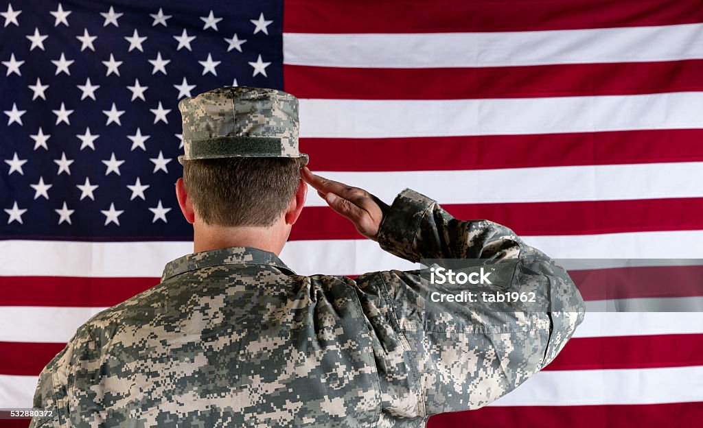 Veteran male solider saluting the flag of USA Male Veteran soldier, back to camera, saluting United States of America flag. Saluting Stock Photo