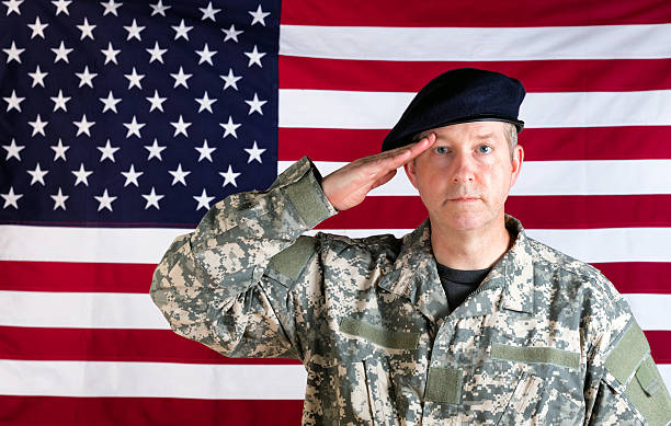 istock Veteran solider saluting with USA flag in background 532880428