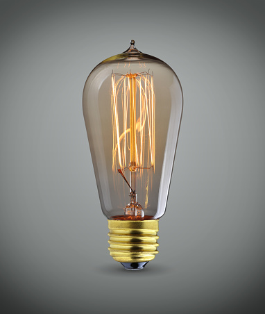 Glowing vintage light bulb over gray background