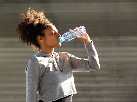 Close up portrait of a young african american sports woman drinking from water bottle