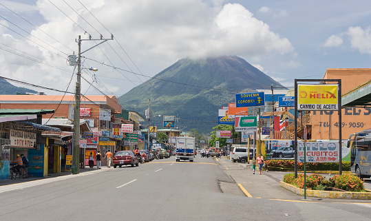 Main street with cars, shops and pedestrians in La Fortuna, Costa Rica. In the background Volcano Arenal, one of the most active volcanos in the world.