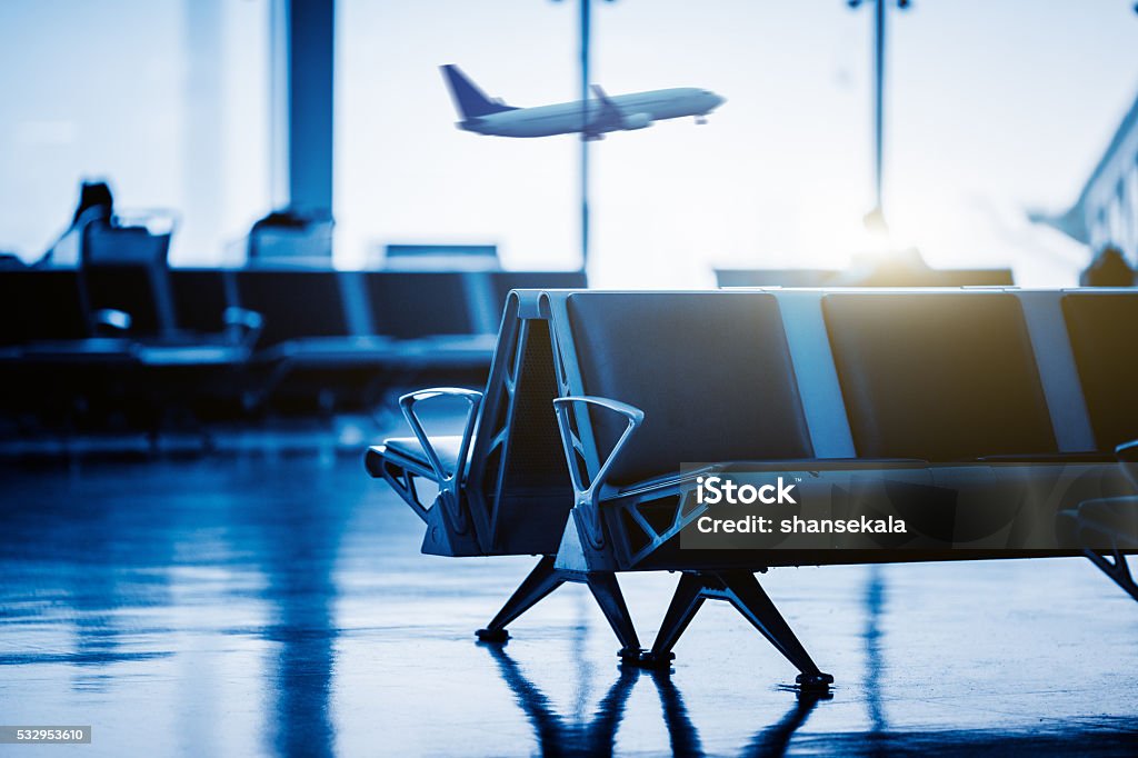 Empty chairs , with airplane flying background Empty chairs in the departure hall at airport , with  an airplane taking off at sunset. blue toned. Airport Stock Photo