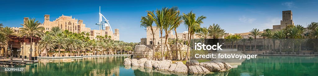 Dubai palm trees lagoon hotels and restaurants Burj panorama UAE The iconic futuristic sails of the luxury Burj Al Arab hotel towering over the traditional wind towers and tranquil palm fringed oasis on the coast of Dubai, United Arab Emirates. ProPhoto RGB profile for maximum color fidelity and gamut. Dubai Stock Photo