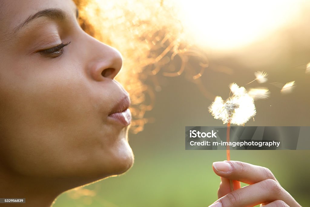 Beautiful young woman blowing dandelion flower Portrait of a beautiful young woman blowing dandelion flower Women Stock Photo