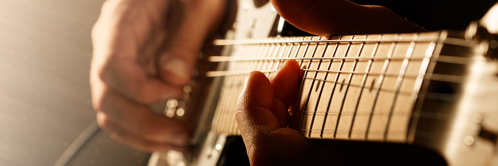 Guitarist holding fret board of guitar playing chord