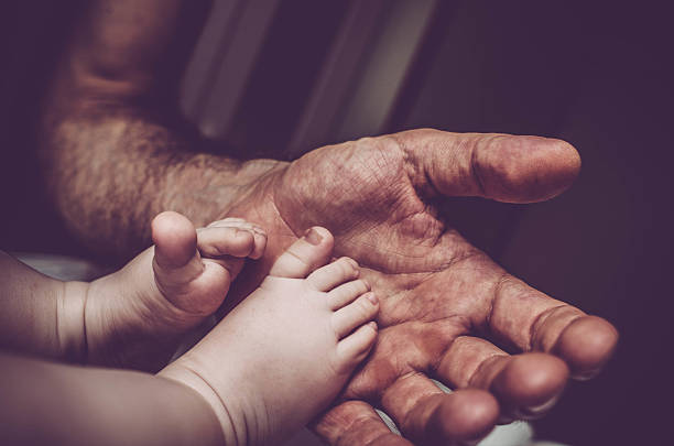 Soft detail, close-up photo of baby´s tiny fingers and feet being gently held in loving palm of their mother, dad´s hand.