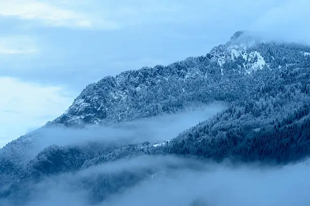 Mountain valley with snow and low clouds.