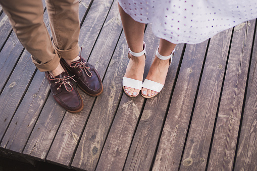 man in brown leather shoes and woman in white open footwear stand side by side on wooden surface