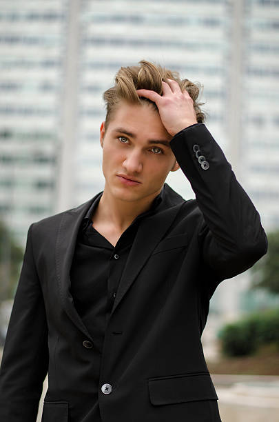 Handsome blond young man outdoor in city setting Handsome blond young man outdoor in city setting, touching hair with his hand, in business suit black men with blonde hair stock pictures, royalty-free photos & images