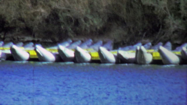 1964: Inflatable river rafting kayaks beached on water banks.