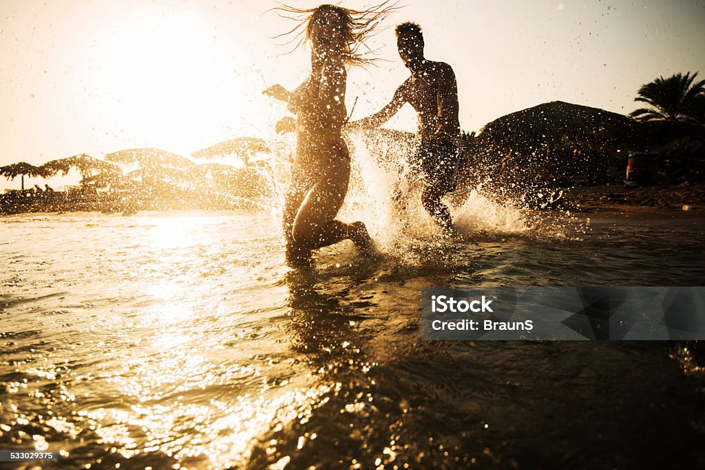 Couple chasing in the sea at sunset. Cheerful couple having fun in summer day at sea. Man is chasing his girlfriend. 2015 Stock Photo