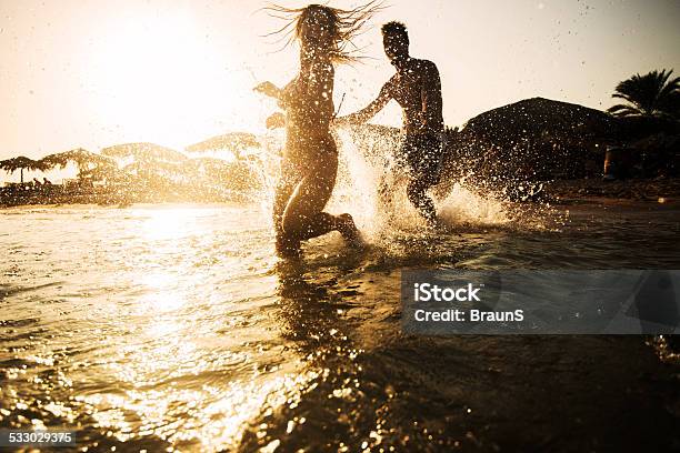 Couple Chasing In The Sea At Sunset Stock Photo - Download Image Now - 2015, Adult, Adults Only