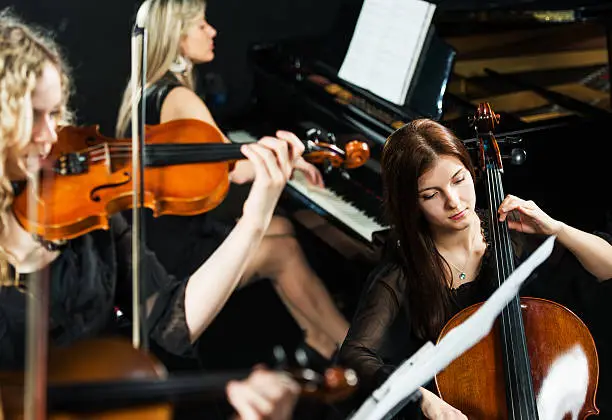 Three women playing cello, piano and violin.