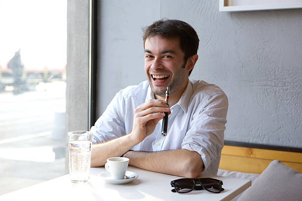 istock Smiling young man sitting indoors with electric cigarette in han 533034651