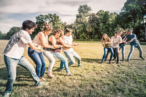 Friends playing tug of war game all together in a park