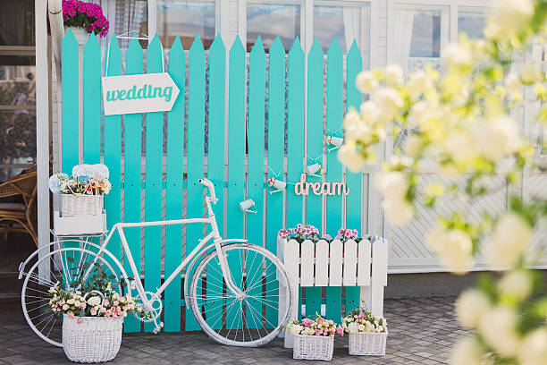 Photo zone for guests at wedding reception. White vintage bicycle, turquoise background, wooden 'wedding' pointer, flowers in baskets, 'dream' sign.