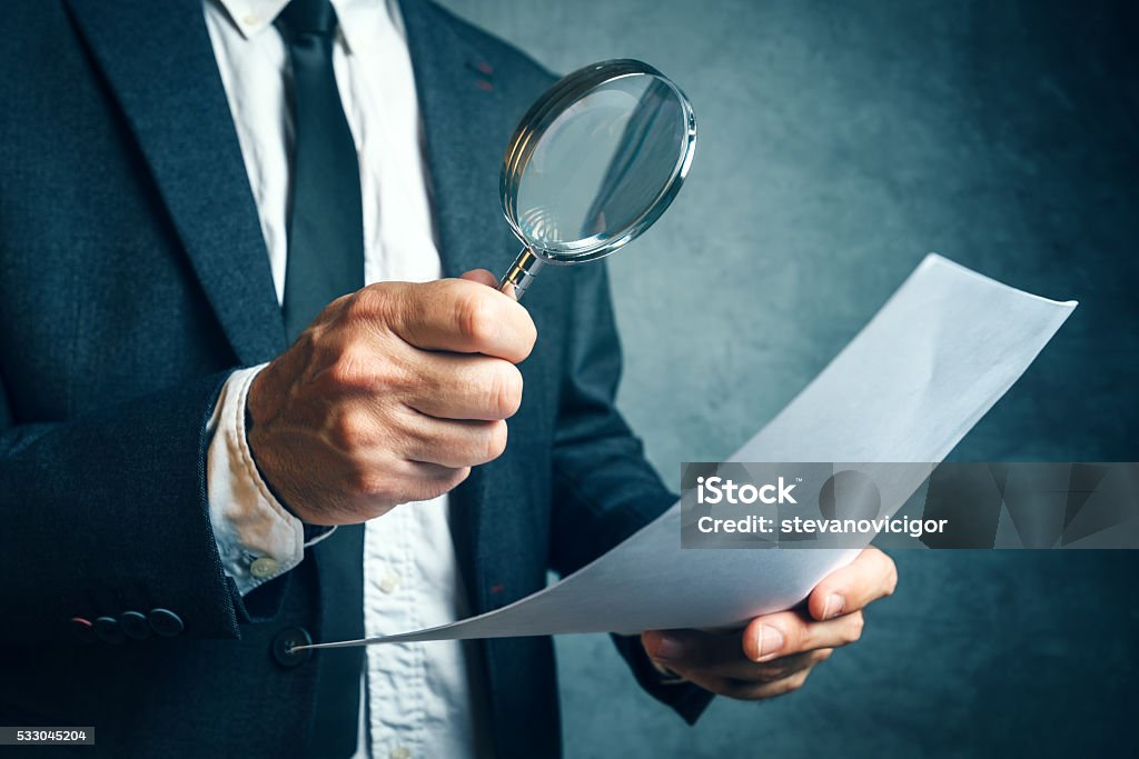 Tax inspector investigating financial documents through magnifyi Tax inspector investigating financial documents through magnifying glass, forensic accounting or financial forensics, inspecting offshore company financial papers, documents and reports. Magnifying Glass Stock Photo