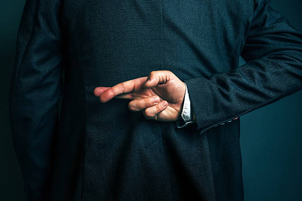 Lying businessman holding fingers crossed behind his back stock photo