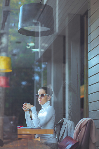 Beautiful, elegant woman enjoying a fresh cup of coffee at cafe. Long dark hair swept back from the face, tied in a bun. Formalwear, sitting, waist up. Copy space has been left.